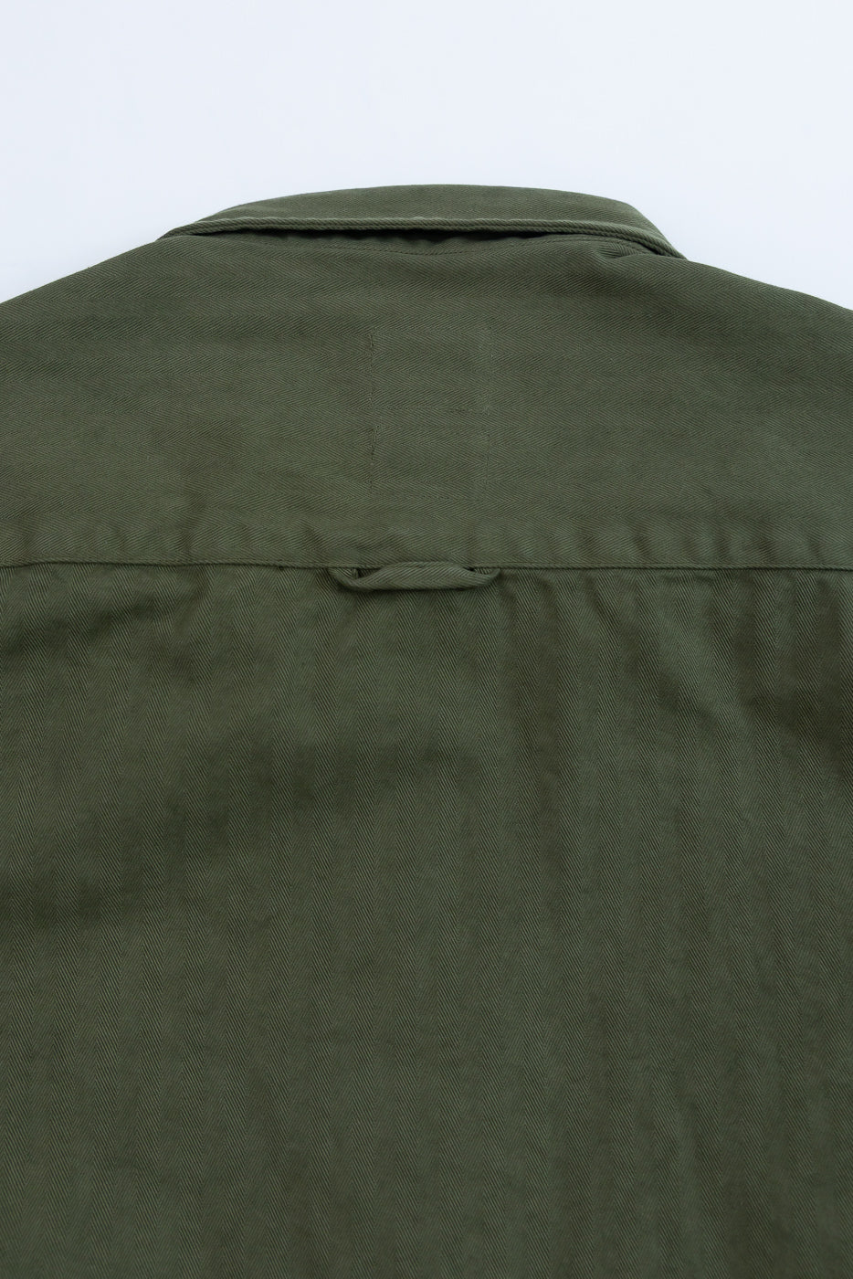 Close-up of the back of an olive green garment showing fabric texture and a locker loop.