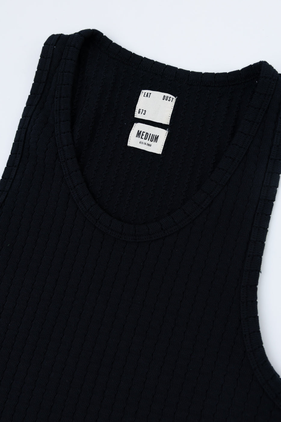Close-up of front upper section of black mesh cotton tank top, ribbed texture, neckline and inner tag detail visible.