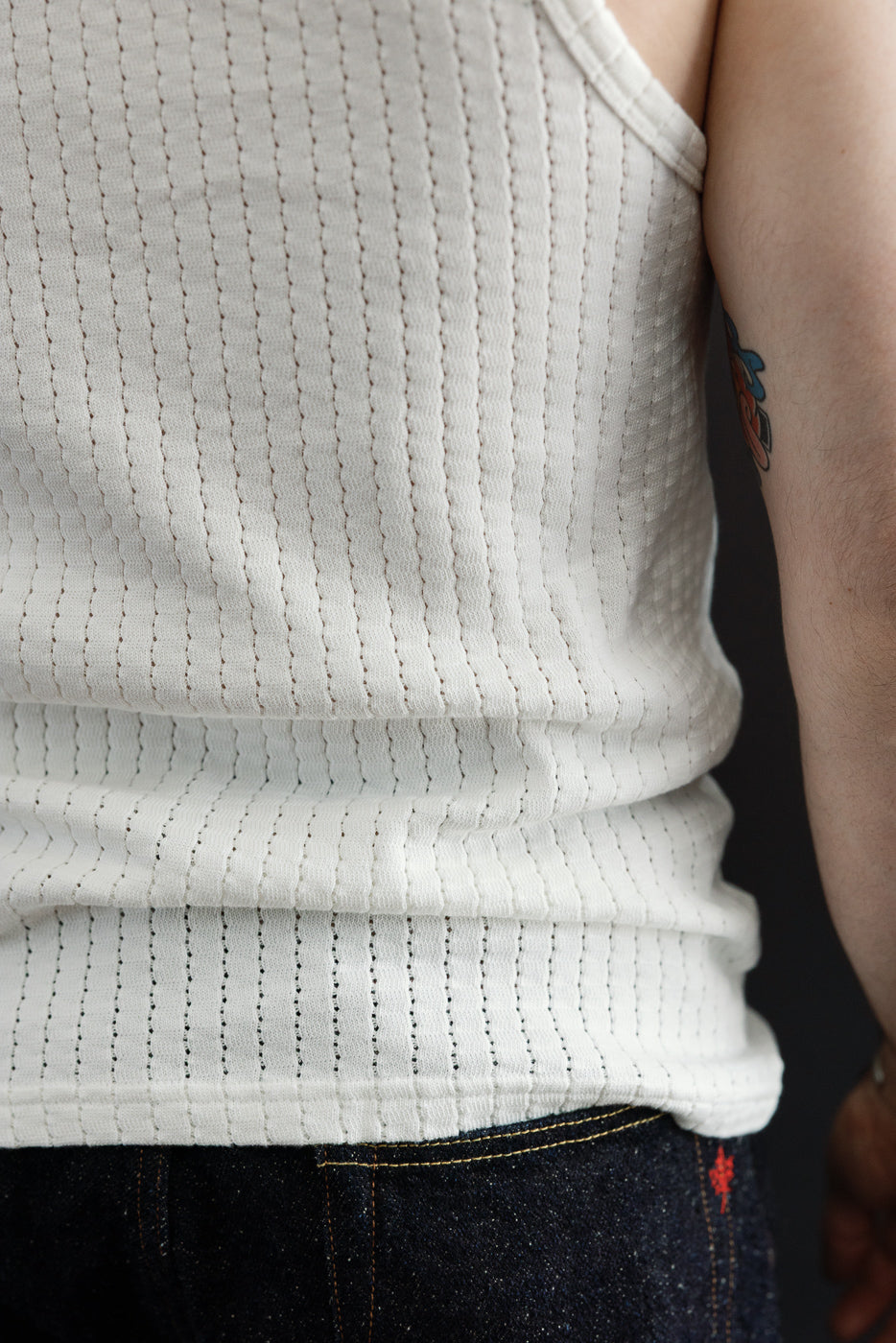 Close-up of male model's side torso wearing white mesh cotton tank top, showing fabric texture; model is 5'9