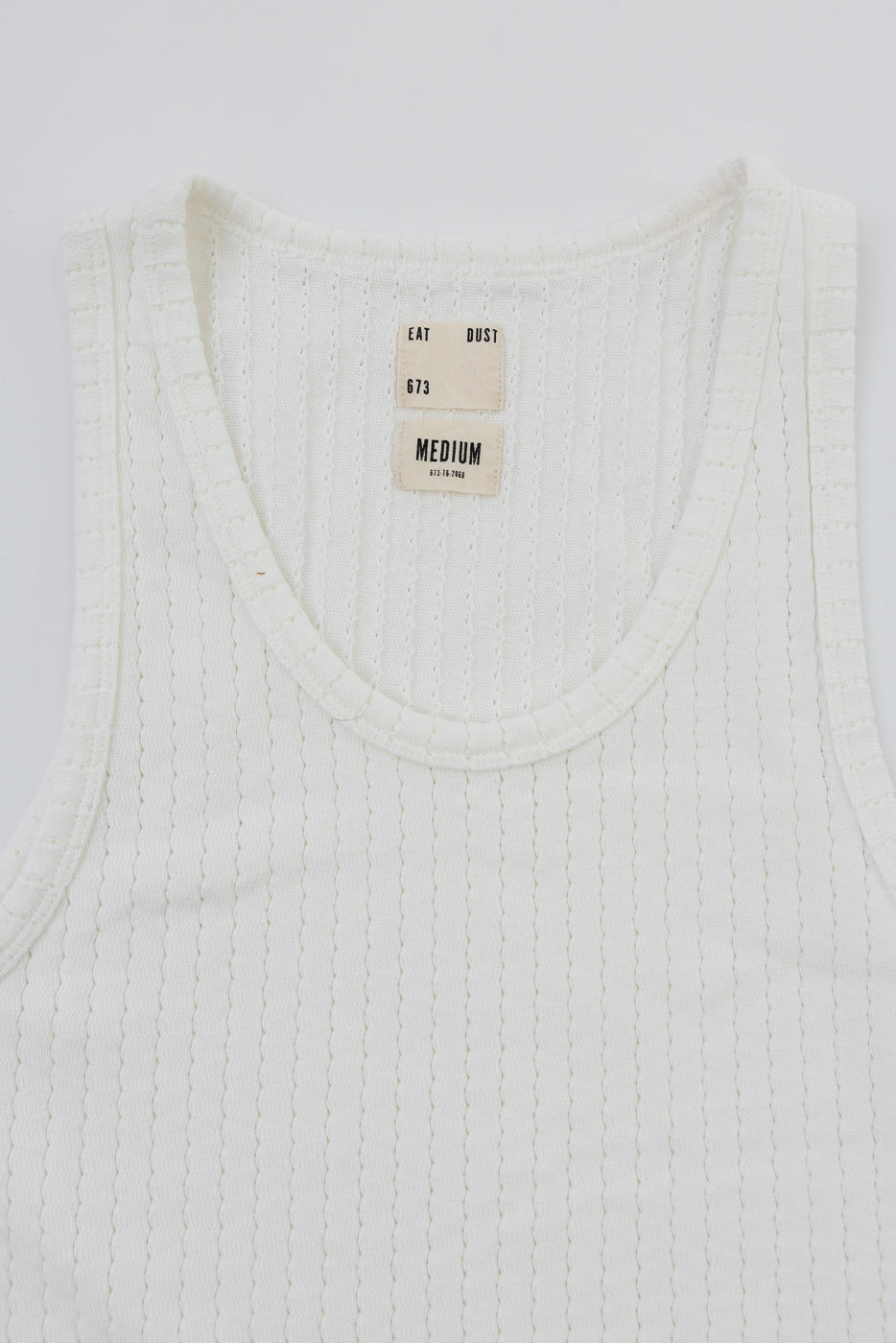 Close-up front view of white mesh cotton tank top, showing ribbed texture and inner neck tags.