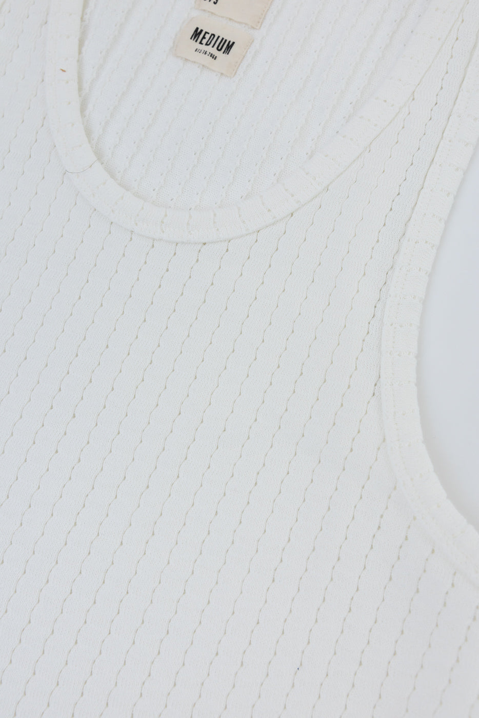 Close-up of front upper chest of ribbed white cotton mesh tank top, showing fabric texture and scoop neckline.
