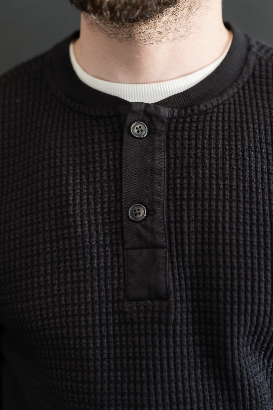 Close-up front view of a male model wearing a black waffle knit henley shirt showing the collar and buttons.