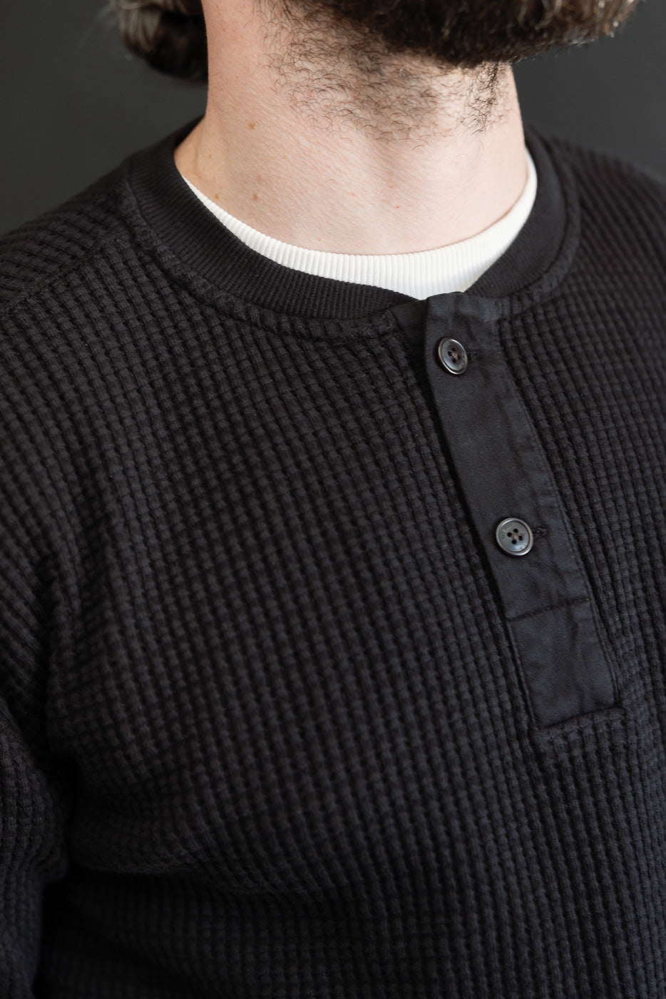 Close-up front view of a black waffle knit henley shirt showing the button placket and texture.