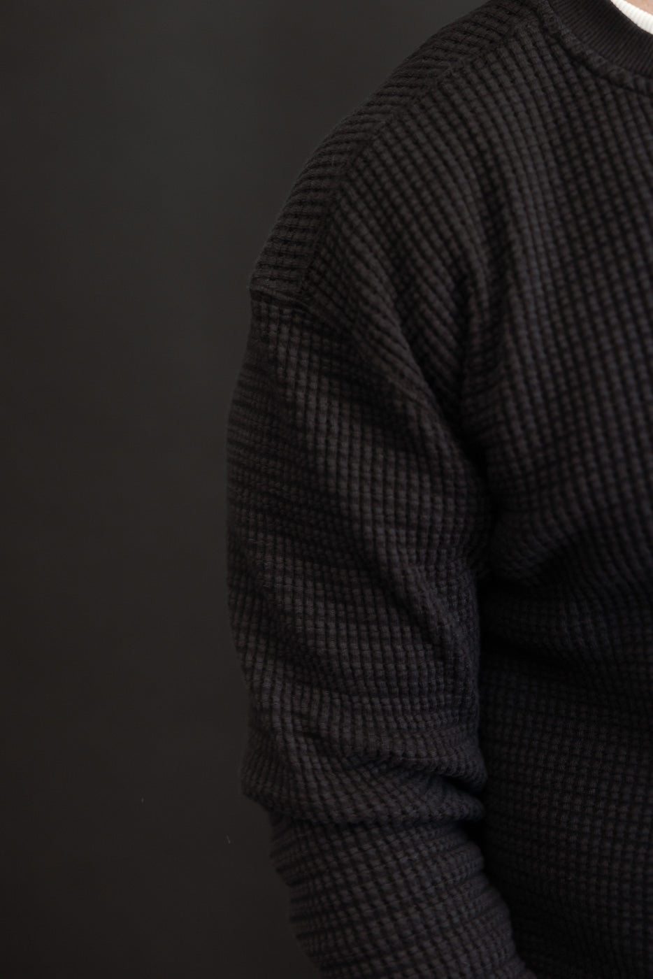 Close-up side view of a black waffle knit thermal long sleeve sweater texture.