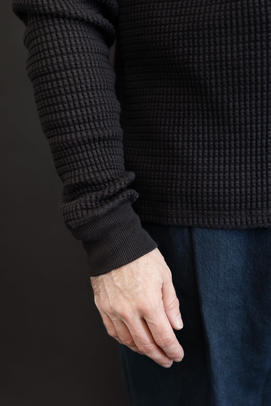 Close-up of the side and sleeve of a black waffle-knit sweater on a male model.