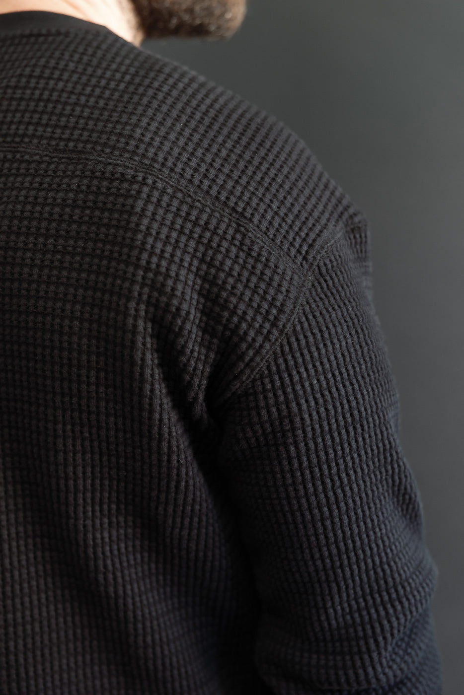 Close-up of the back and shoulder of a black waffle knit thermal long sleeve shirt.