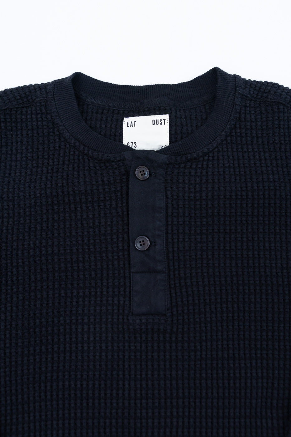 Close-up front view of a navy waffle knit henley shirt showing button placket and collar detail.