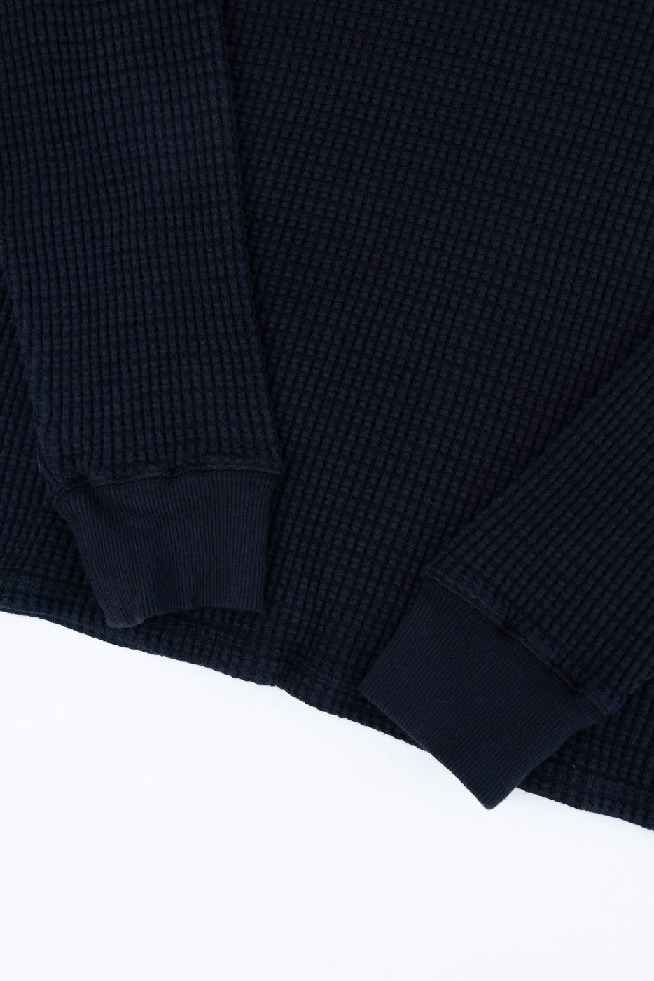 Close-up of the front waffle knit texture and ribbed cuffs of a navy blue long-sleeve shirt.