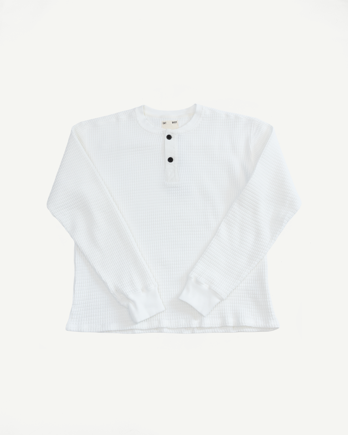 Flat lay front view of a white waffle knit long sleeve henley shirt with black buttons.