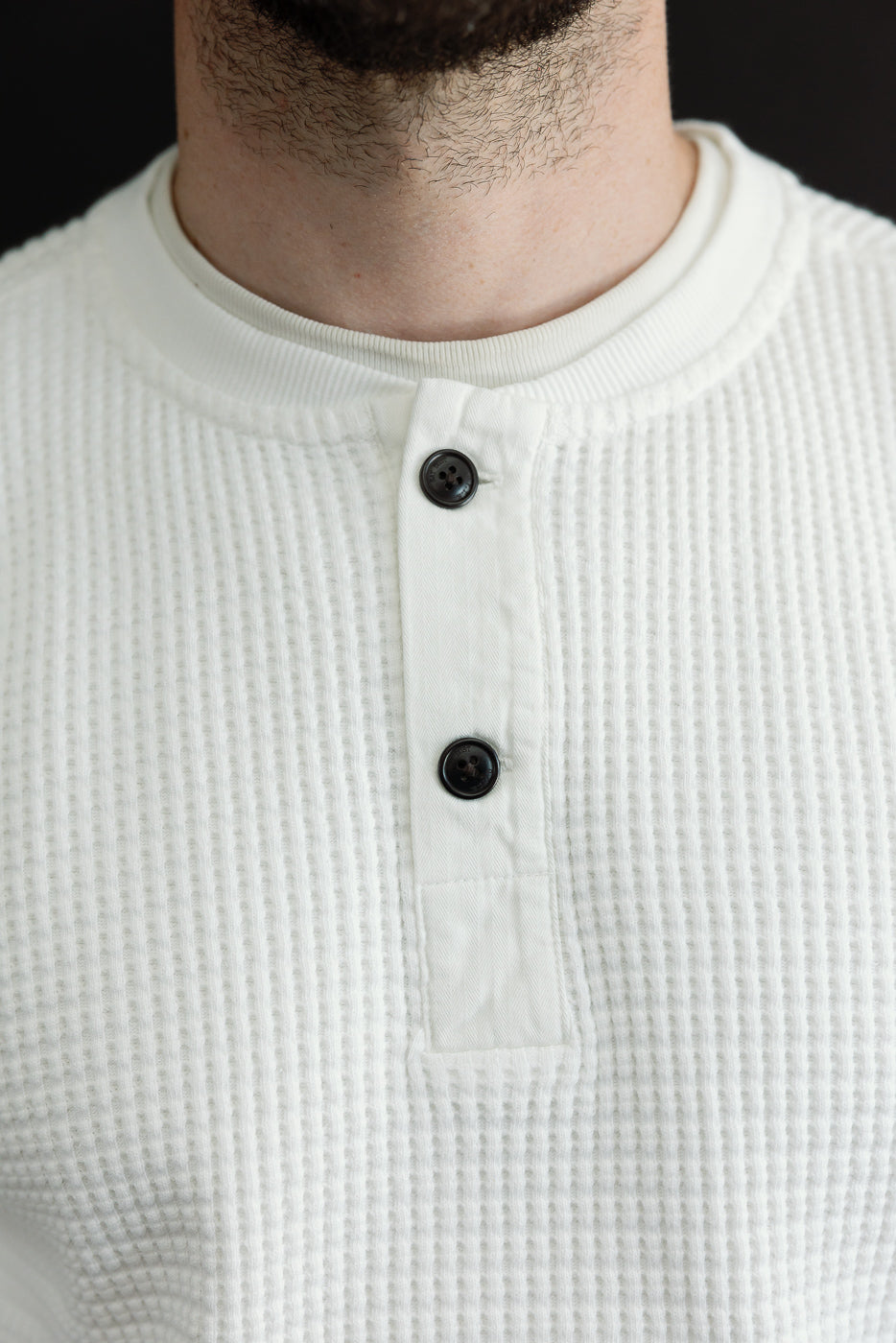 Close-up front of a white waffle knit henley with buttons on a male model, 5'9