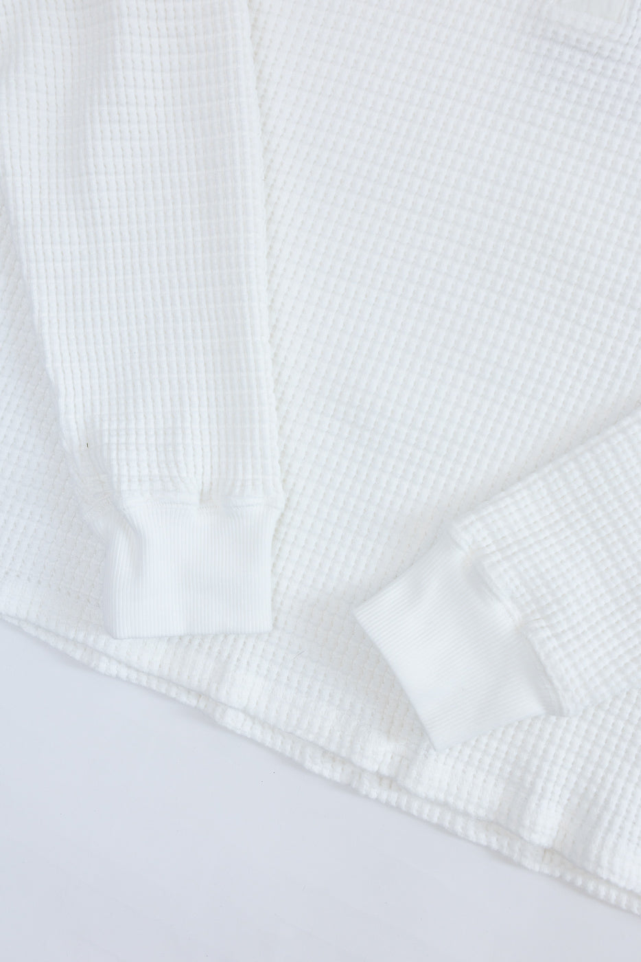 Close-up of the front white waffle knit fabric and ribbed cuffs of a long-sleeve shirt.