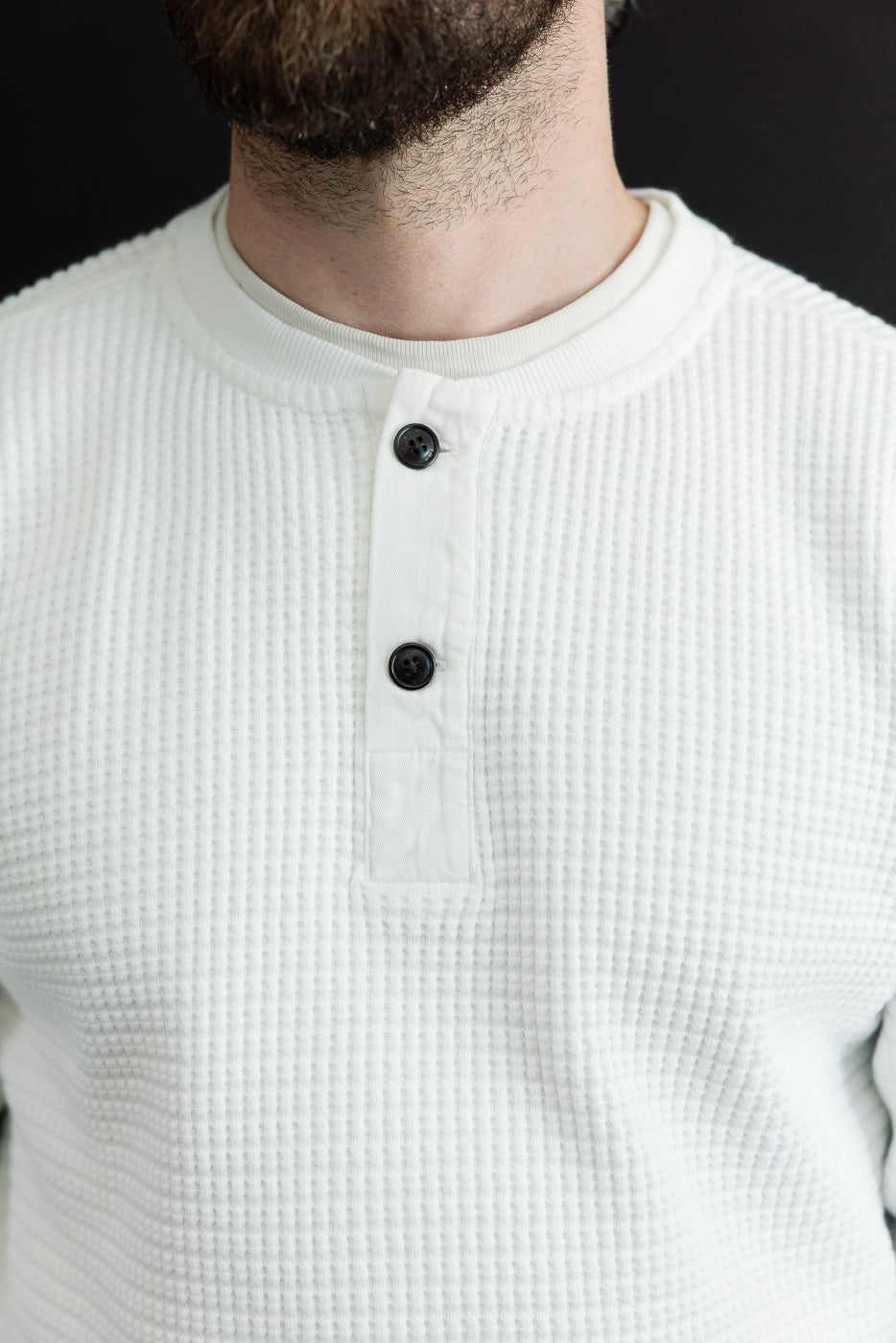 Close-up front view of a white waffle-knit Henley with dark buttons on a male model, 5'9