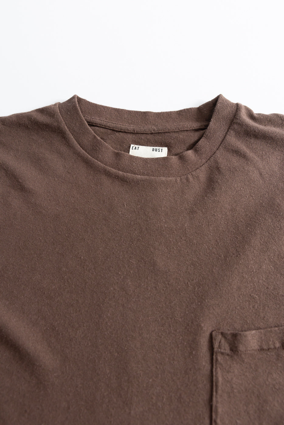 Close-up of front chest area of brown cotton hemp pocket t-shirt, shows tag and fabric texture.