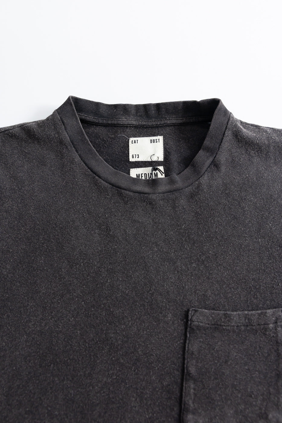 Close-up of front chest area of vintage black cotton hemp pocket t-shirt, showing collar, fabric texture, left chest pocket, and neck tags.
