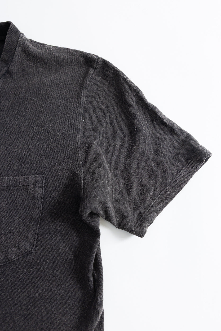 Close-up of front left chest and sleeve of vintage black cotton hemp pocket t-shirt, fabric detail visible.