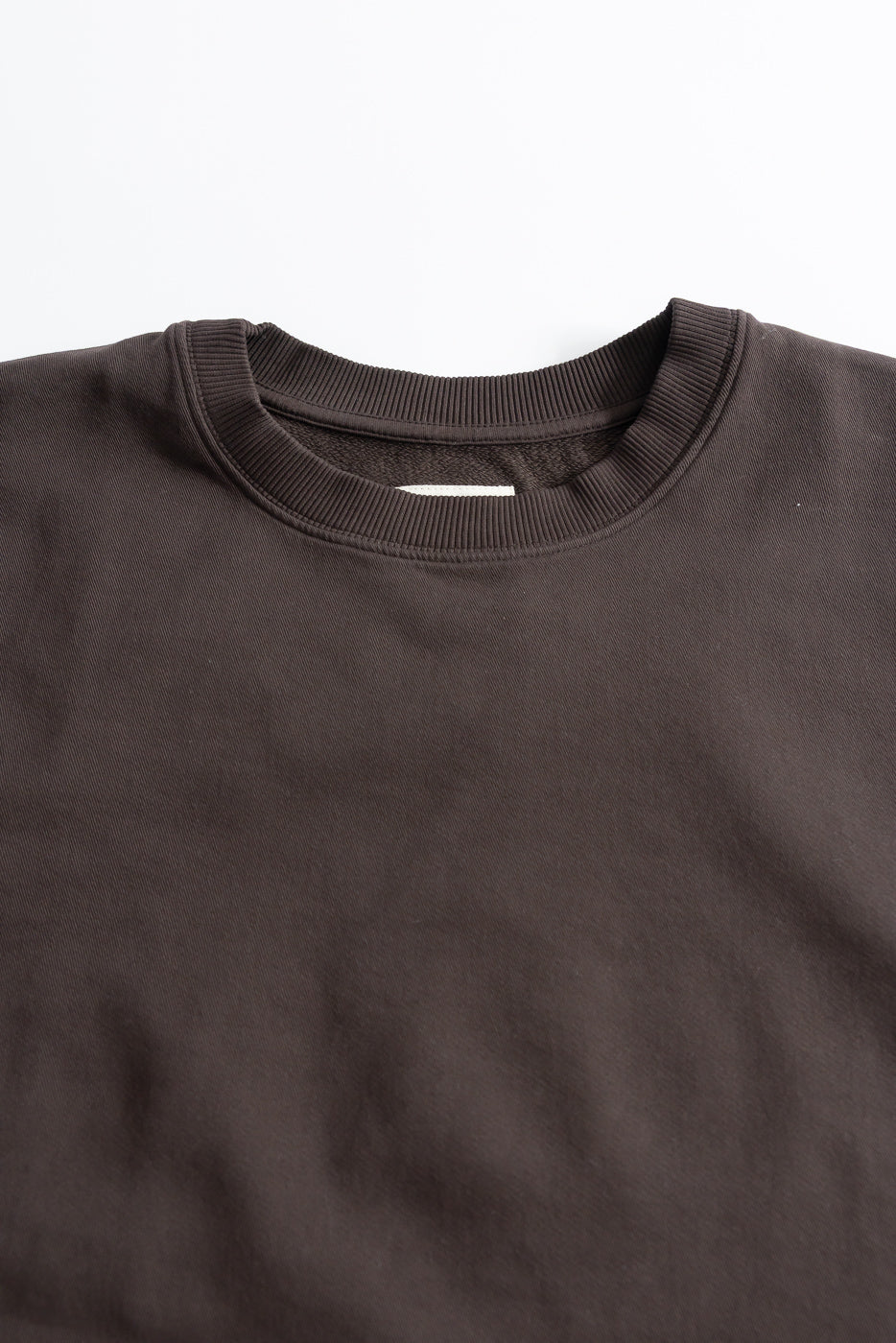Close-up of front chest and collar of brown twill crewneck t-shirt, showing fabric texture and ribbed neckline.