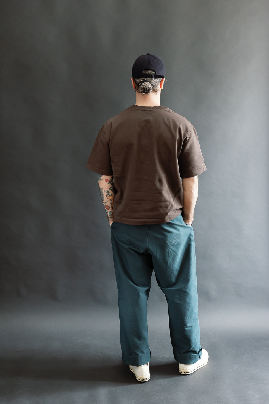 Full body rear view of male model 5'9 165lbs wearing brown short sleeve t-shirt and blue pants