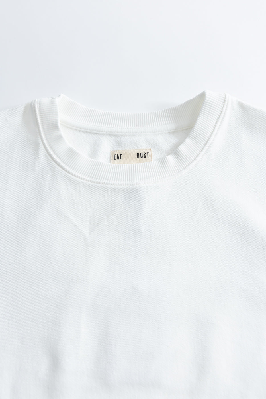 Close-up of white crewneck t-shirt front, ribbed collar, visible neck tag, cotton twill fabric