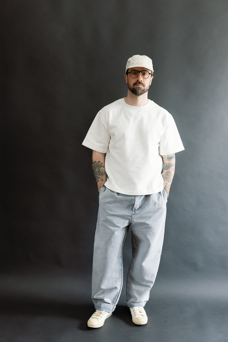 Full body front view of male model 5'9, 165lbs, athletic build, in white short sleeve tee and light blue loose fit pants.