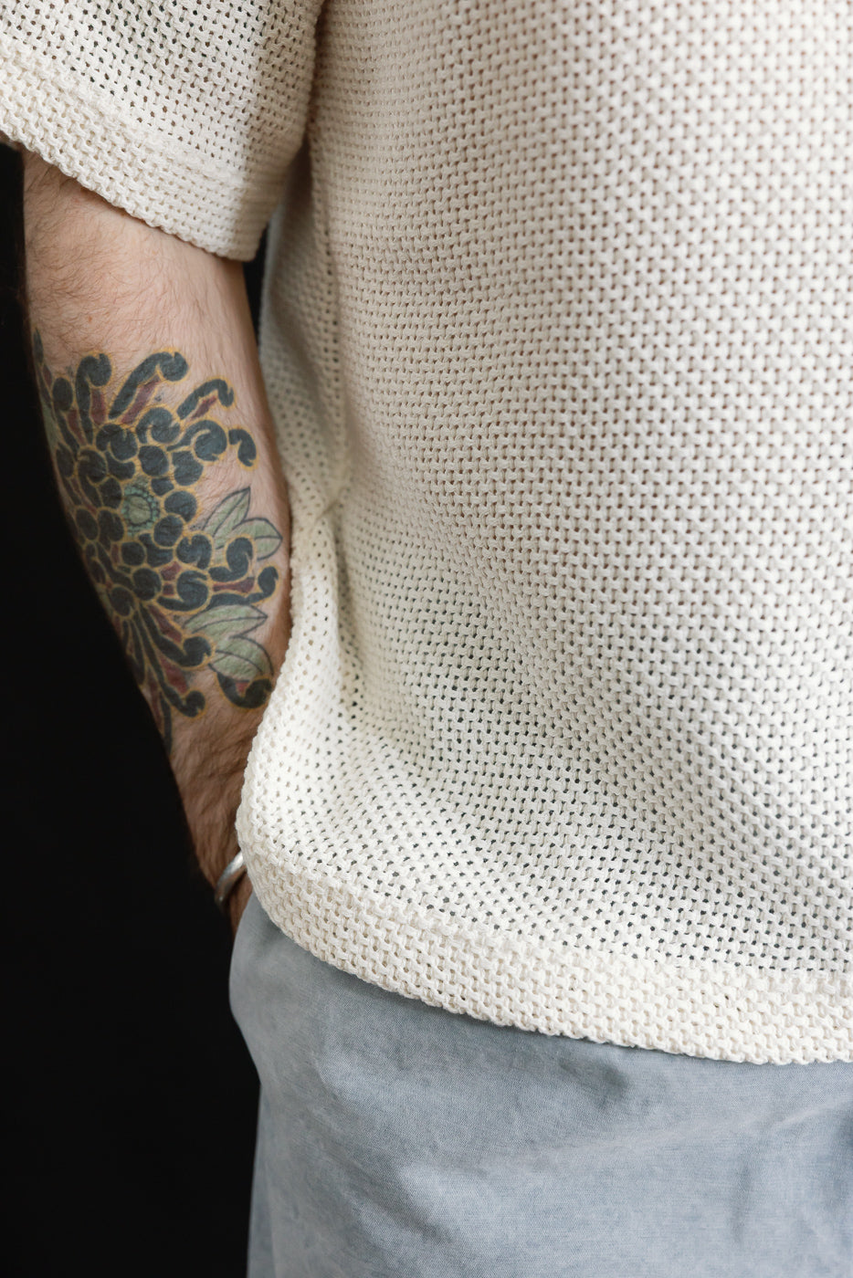 Close-up of male model's side torso wearing ecru cotton textured knit T-shirt, hem and sleeve details visible, model is 5'9