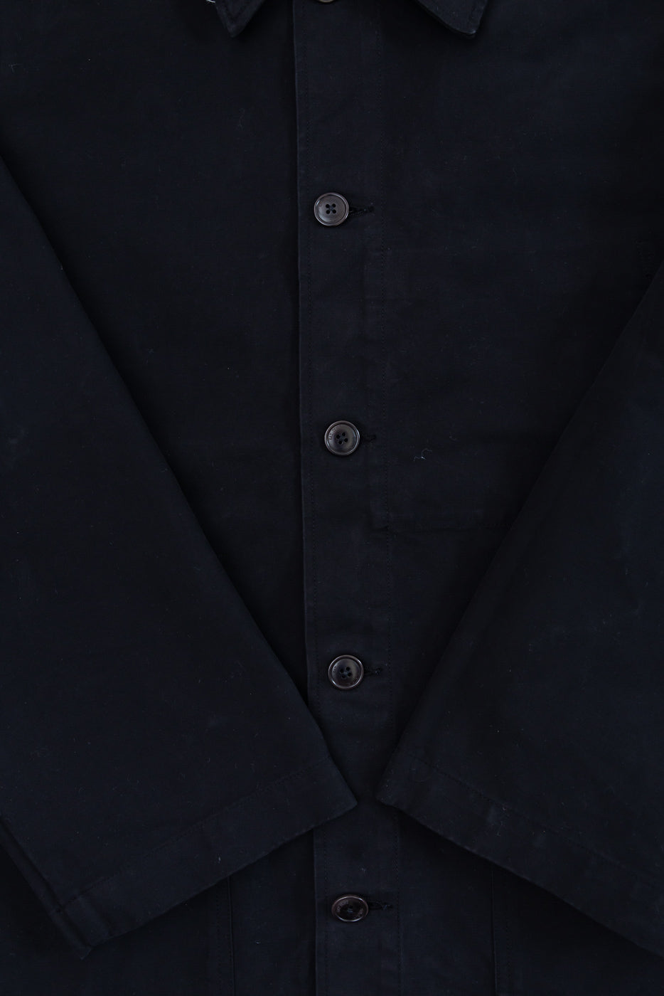 Close-up front view of black fabric texture and dark buttons on a casual jacket.