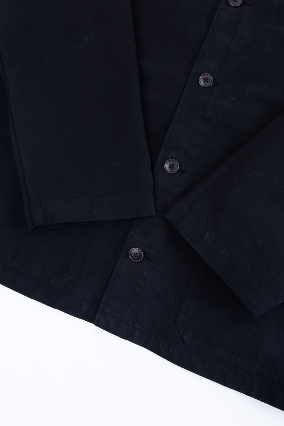 Close-up front view of black cotton jacket showing button details and fabric texture.