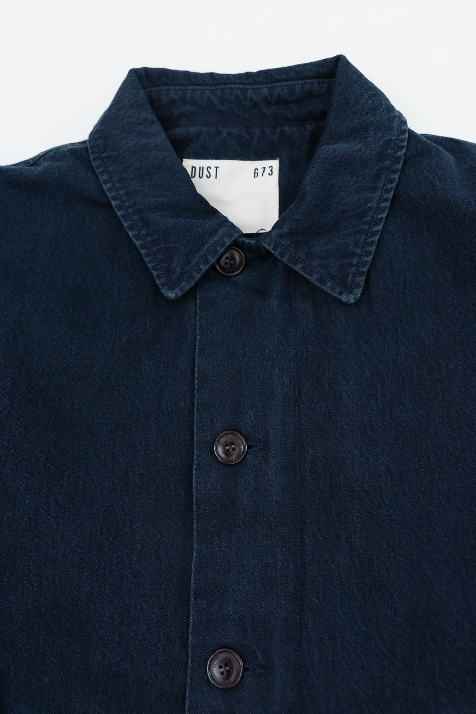 Close-up front view of navy blue fabric texture, collar, and button details on a shirt.