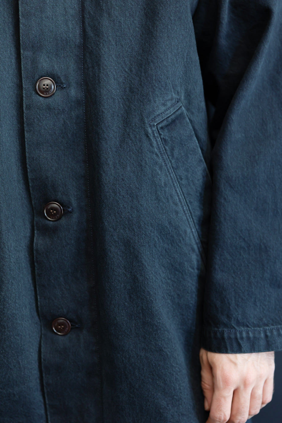 Close-up of the front side and pocket detail of a dark navy textured fabric coat.
