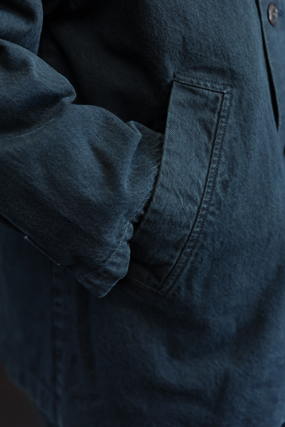 Close-up of the side pocket and fabric texture on the front of a dark denim jacket.