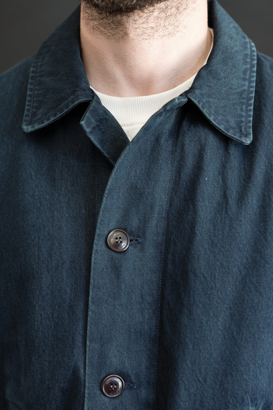 Close-up front view of a male model wearing a dark navy blue cotton chore coat, showing the collar and buttons.