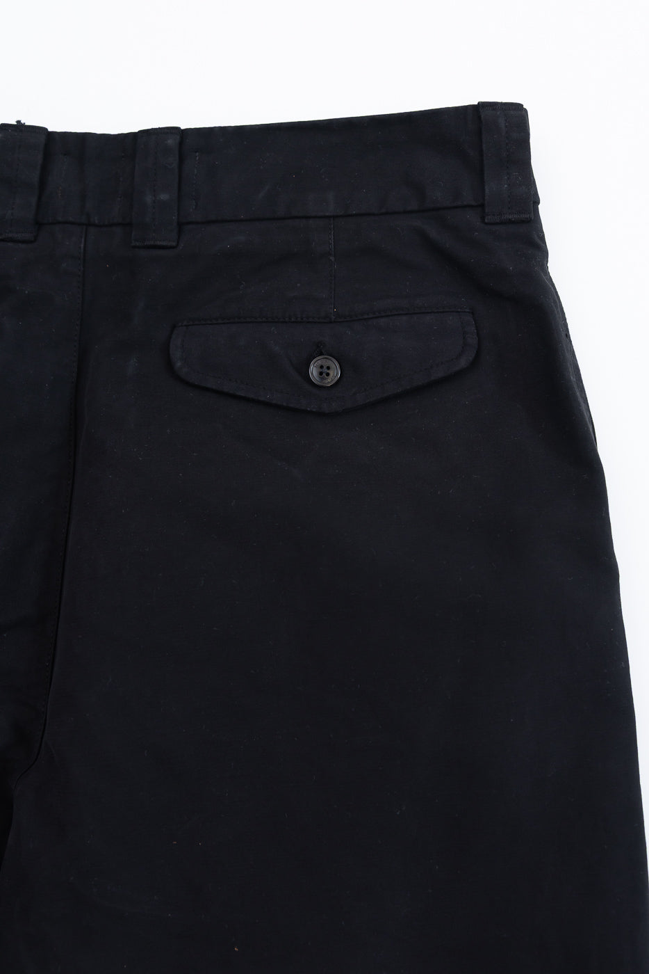 Close-up of the back right pocket of black casual trousers featuring a buttoned flap detail.