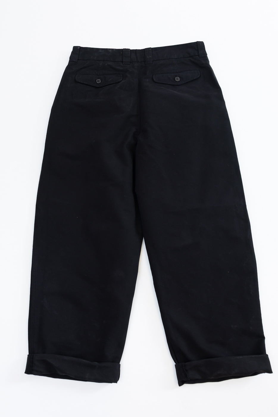 Back view flat lay of black trousers featuring rear button pockets and cuffed hems.