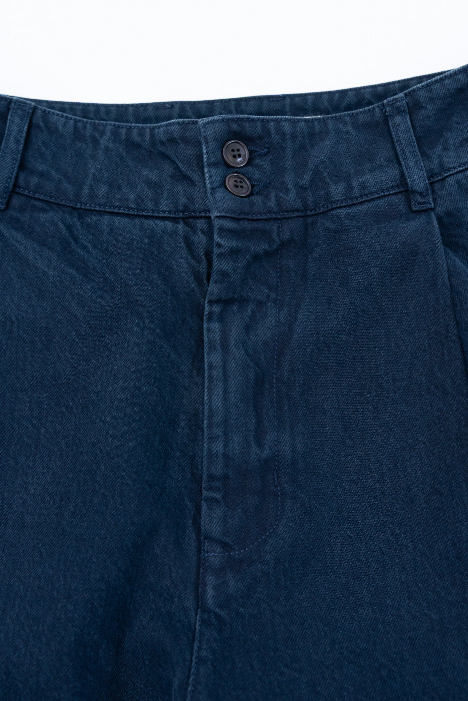 Close-up of the front waist and double-button closure of navy blue denim trousers.