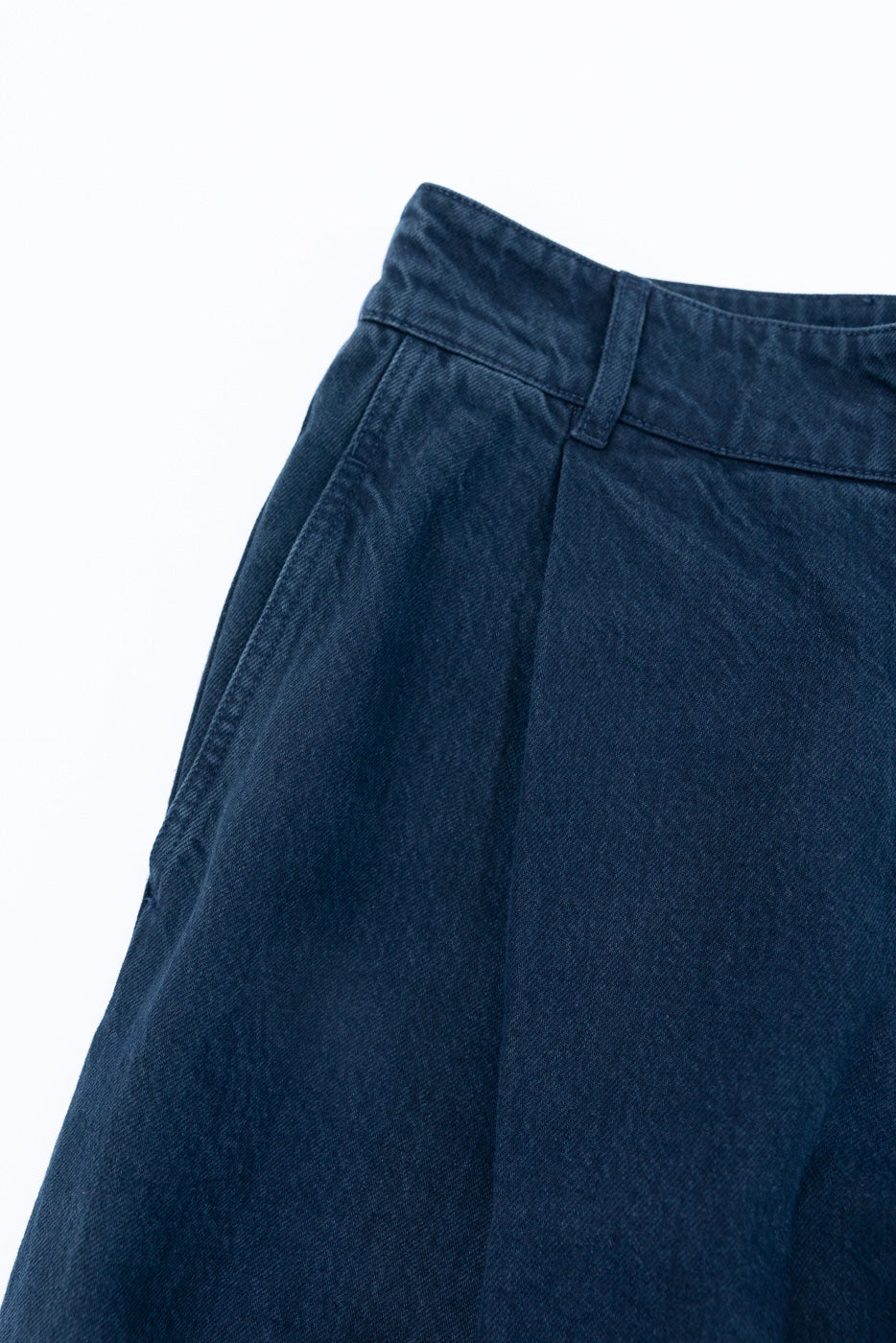 Close-up of the front waistband and pocket detail on navy blue denim trousers.