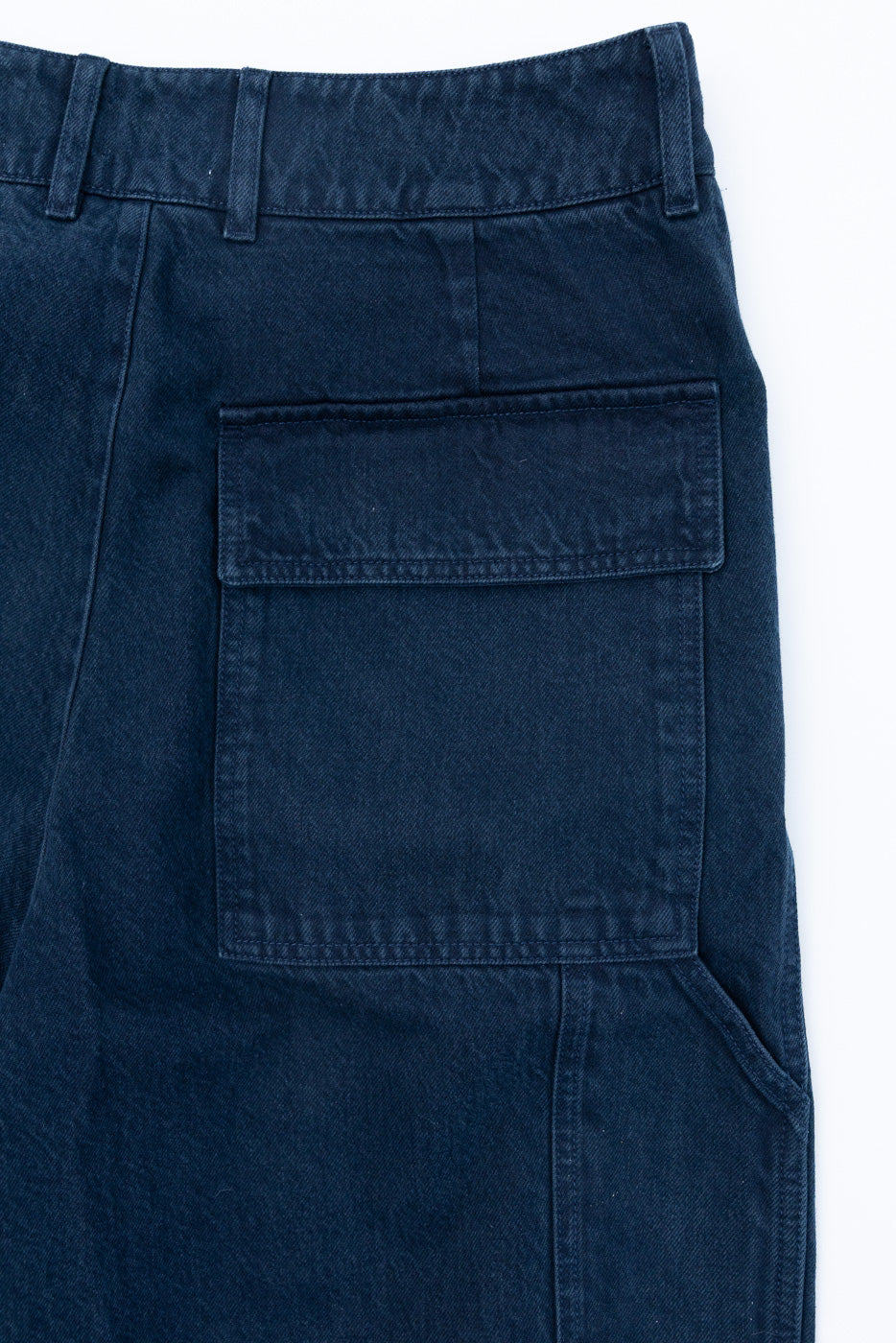 Close-up front view of a navy blue cargo pocket with flap detail on cotton twill trousers.