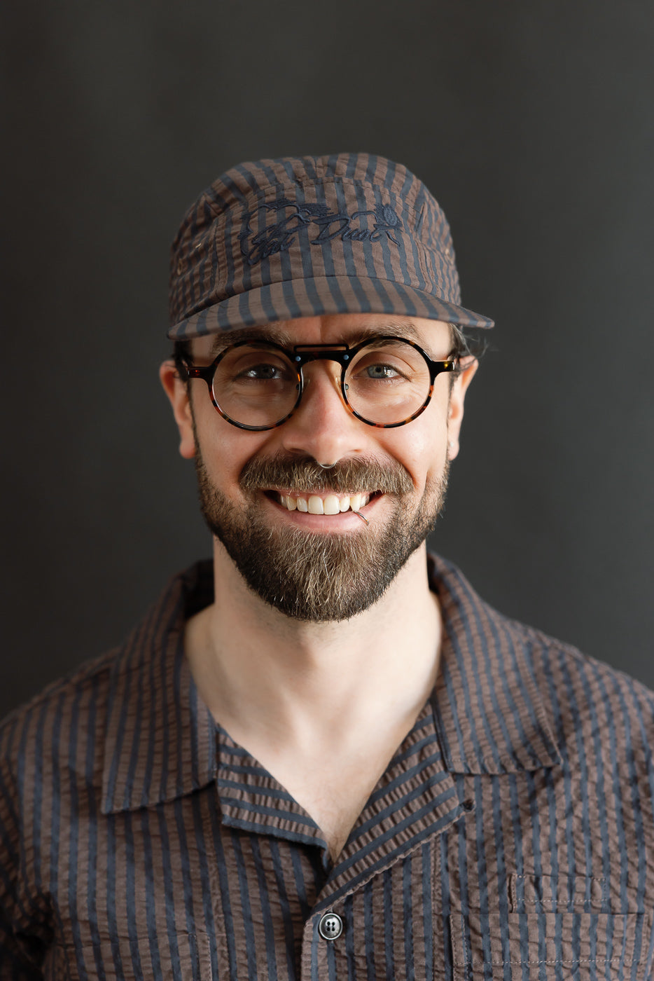 Male model 5'9 165lbs athletic build wearing coffee navy seersucker 5-panel cap, close-up front view shows cap fabric texture and front panel detail