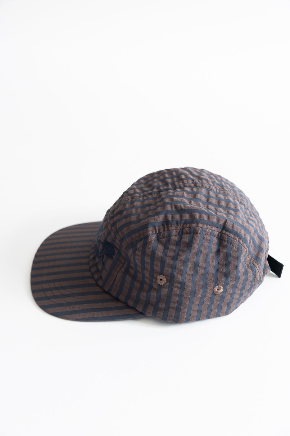 Flat lay of front and side of navy and coffee striped 5-panel cap, seersucker fabric, vent eyelets visible.