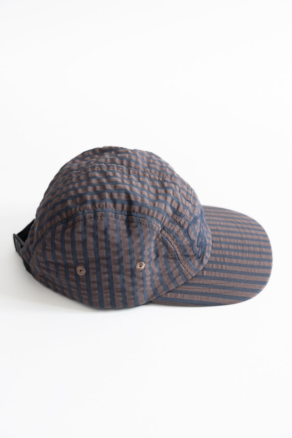 Close-up side view of a navy and coffee striped 5-panel cap, textured seersucker fabric.