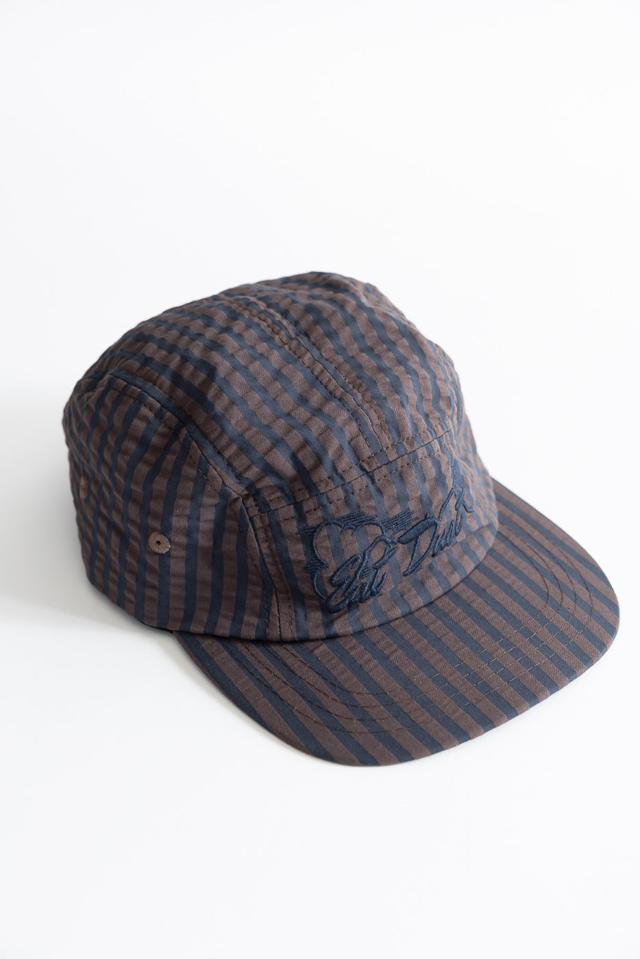 Close-up front view of coffee and navy striped 5-panel cap showing embroidered logo and seersucker fabric texture.