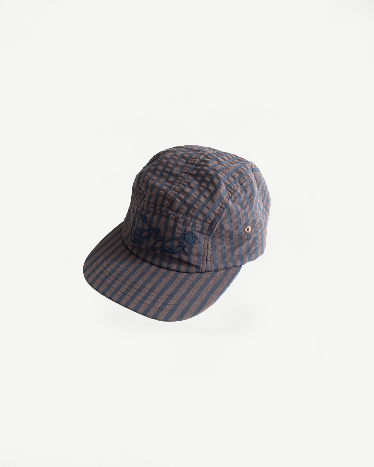 Front angled flat lay of navy and coffee striped seersucker 5-panel cap, detailing embroidery and brim.