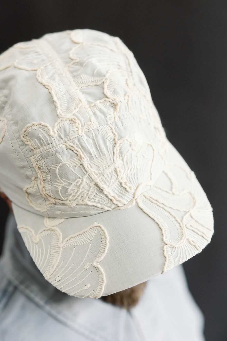 Close-up of front and top of cream cotton 5-panel cap with intricate embroidery, worn by male model, 5'9