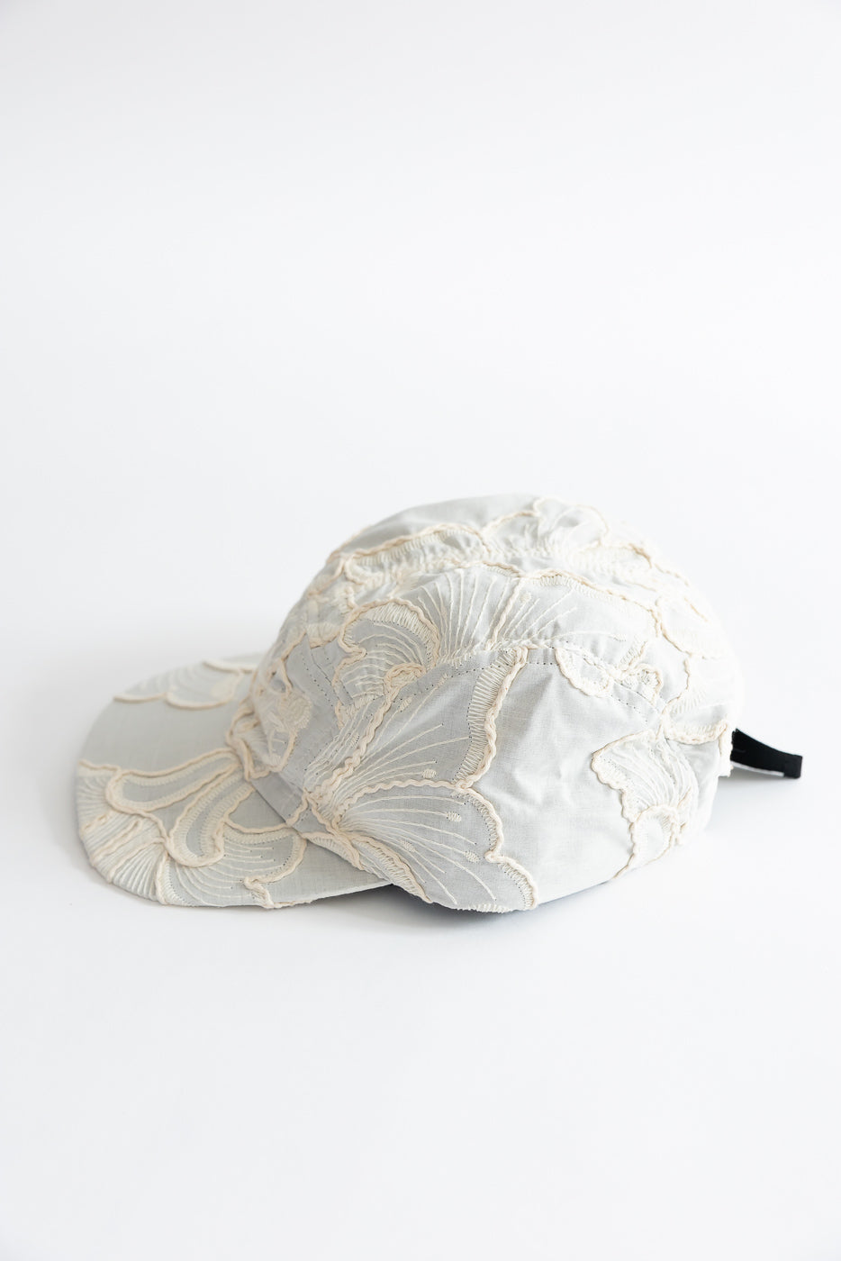 Flat lay side view of 5-panel cap in wheat-colored cotton with embroidered floral texture