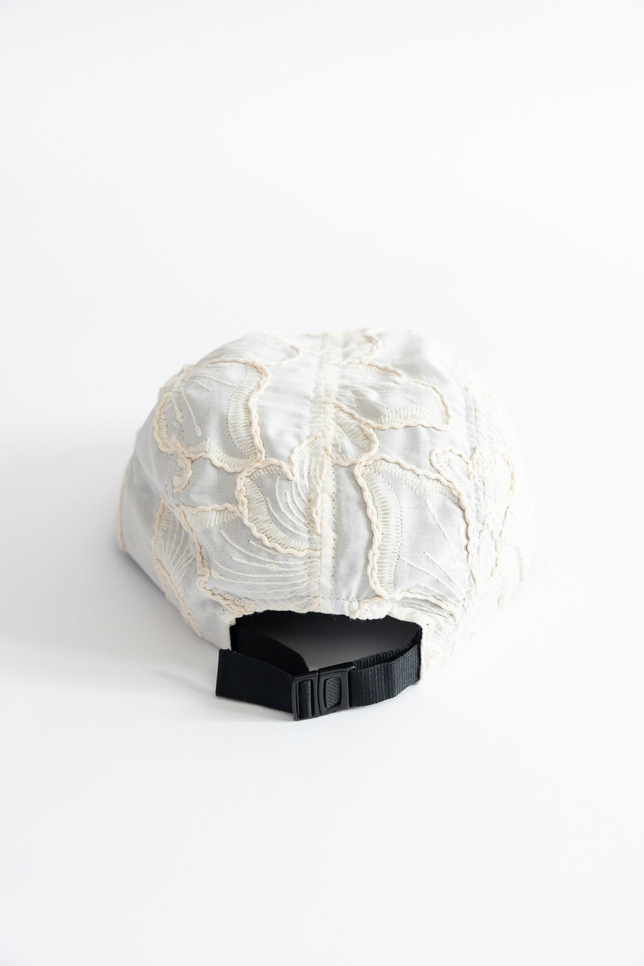 Close-up of back side of a beige embroidered cotton 5-panel cap with black adjustable strap