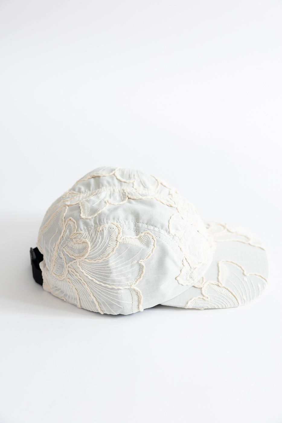 Side view close-up of cream cotton 5-panel cap with embroidered floral texture and adjustable strap