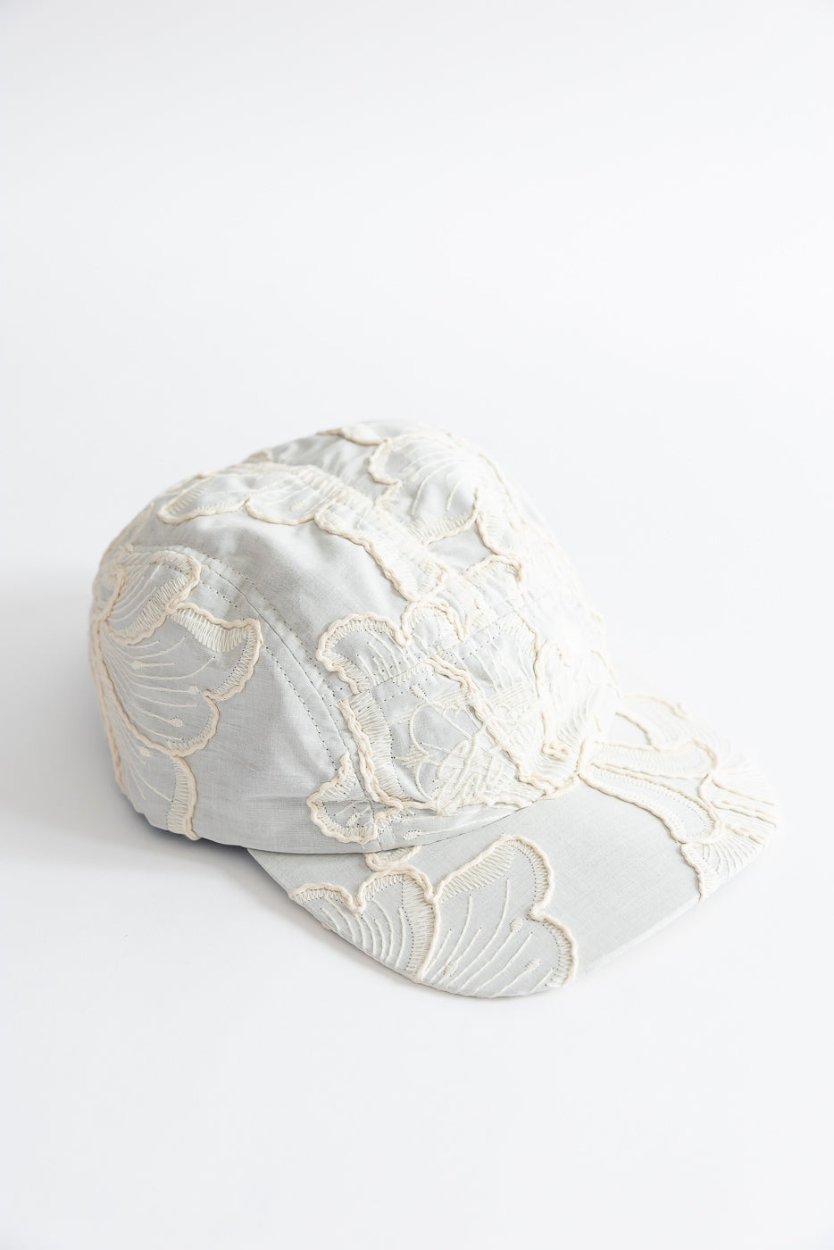 Close-up front view of a wheat-colored 5-panel cap with floral embroidery details.