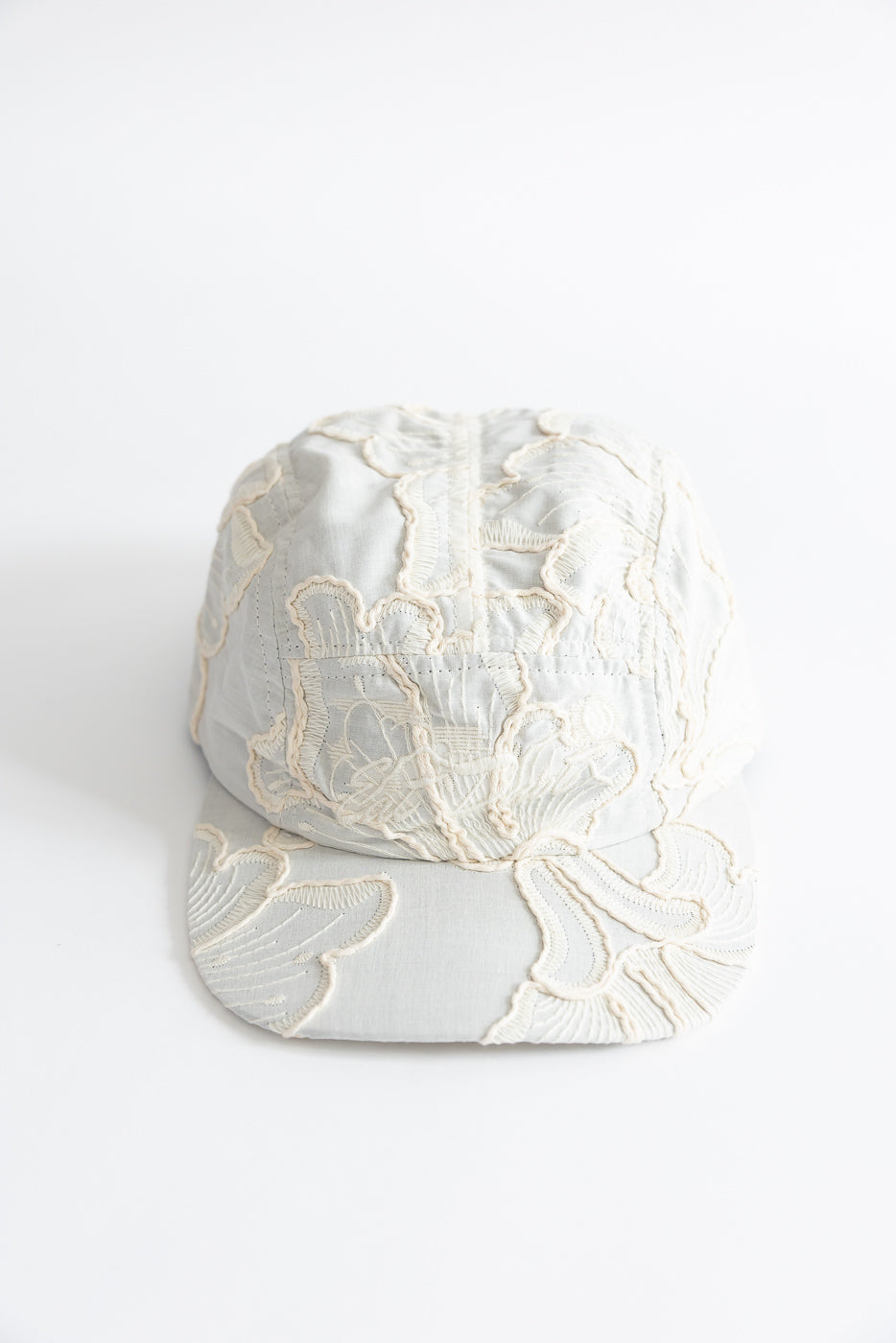 Front close-up view of a wheat-colored cotton 5-panel cap with floral embroidery detail.