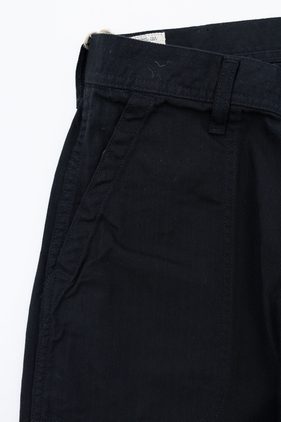 Close-up front view of black herringbone chinos showing waistband, belt loop, and fabric texture