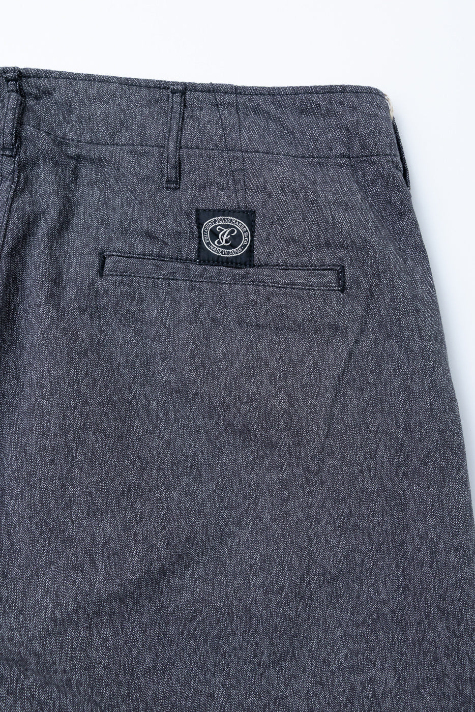 Close-up back view of dark selvedge chino pants showing rear pocket, woven label, and textured fabric detail