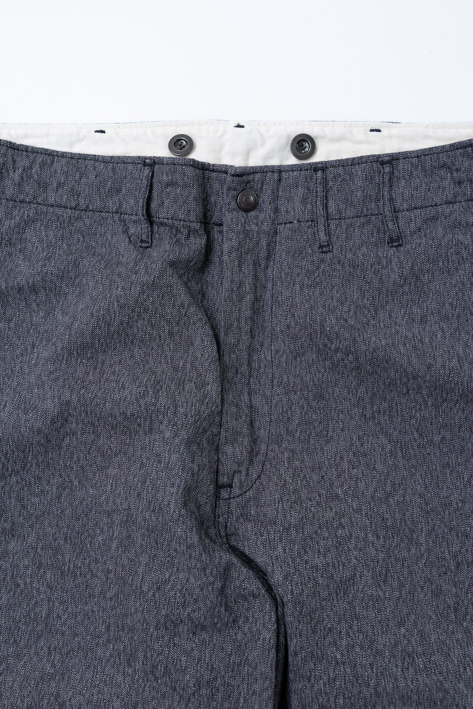 Close-up front view of dark denim pants with button fly and white waistband lining