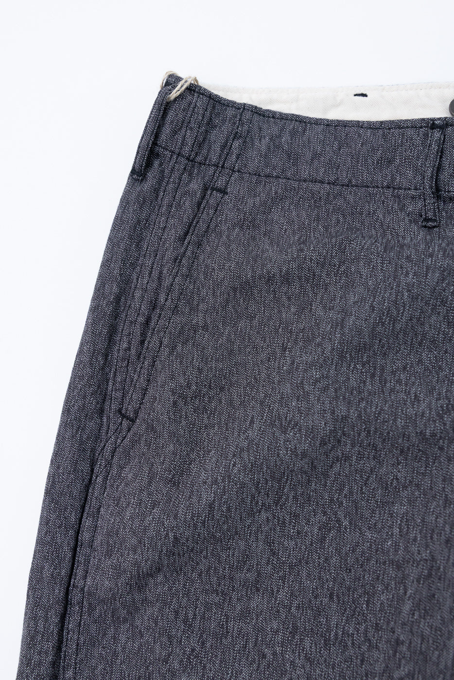 Close-up front view of dark selvedge denim pants, showcasing texture, stitching, and waistband detail.